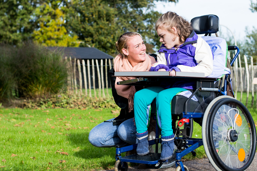 Disabled child in wheelchair improving emotional wellbeing through disability friendly animal interactions with the help of a care assistant